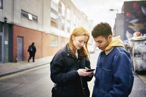 Woman and man standing in a street both looking at her phone.